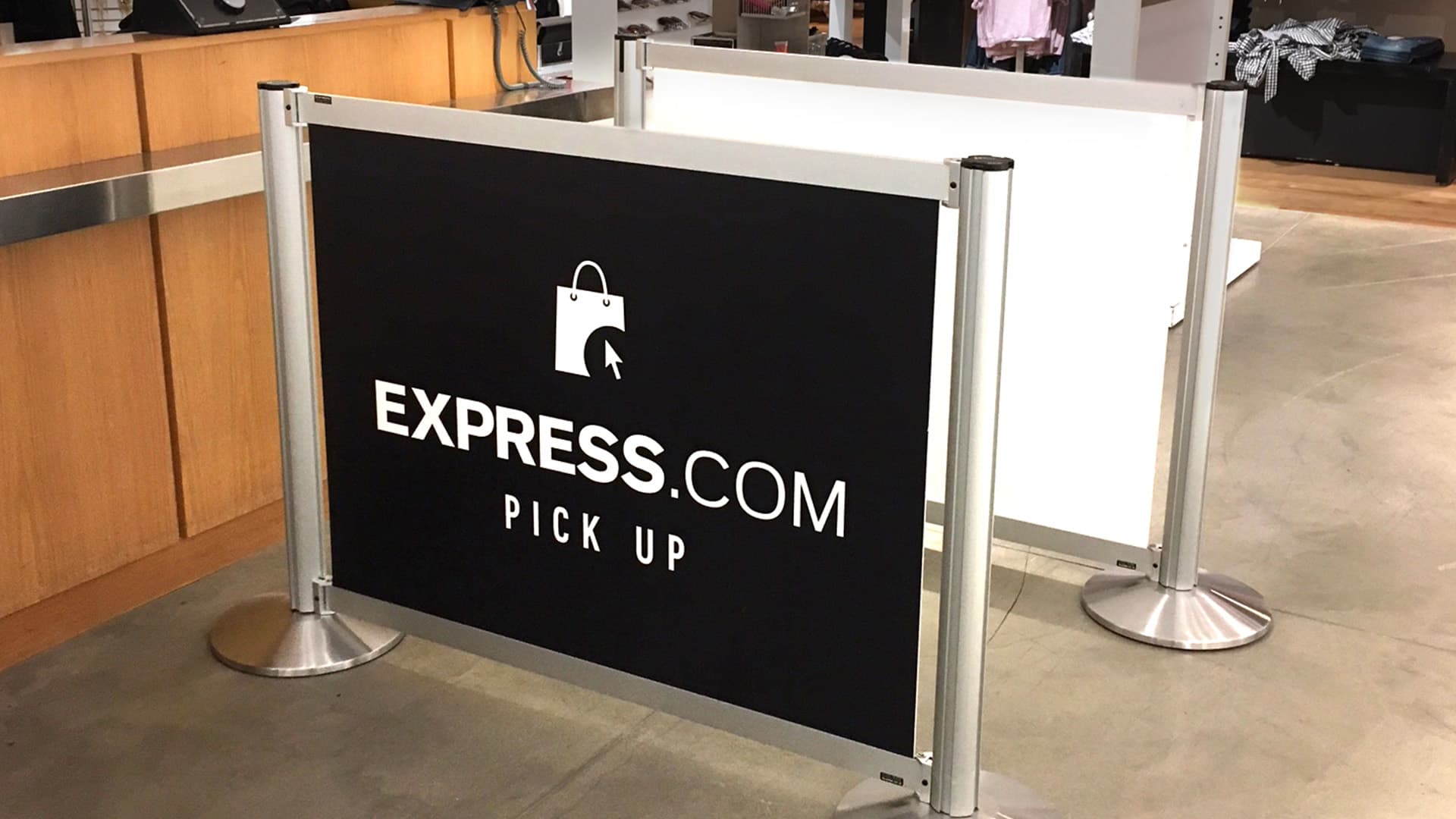 Post and Panel barriers with Express branded graphics guide shoppers to the pickup counter in an Express store.