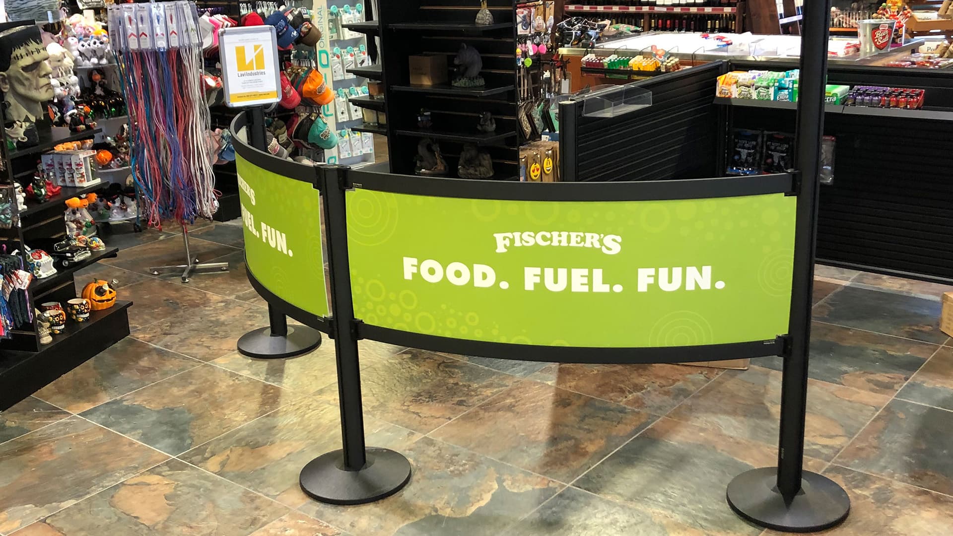 Rigid Rail barriers with Fischer's branded graphics guide customers through the checkout queue at a convenience store.