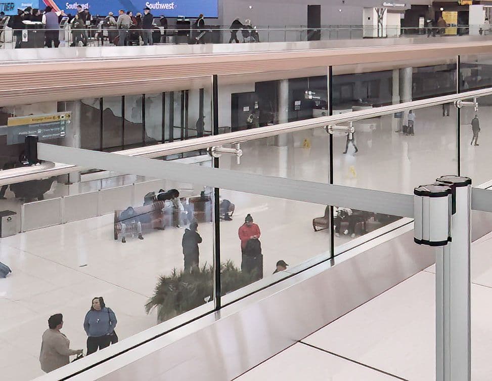 A glass-mount retractable belt safety barrier blocks access at a guardrail inside Denver International Airport.