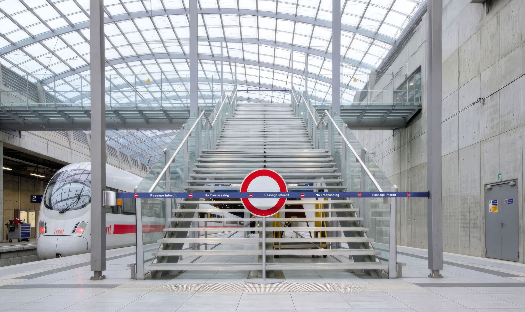 A wall-mounted retractable belt safety barrier blocks access to a stairway inside a transit station.