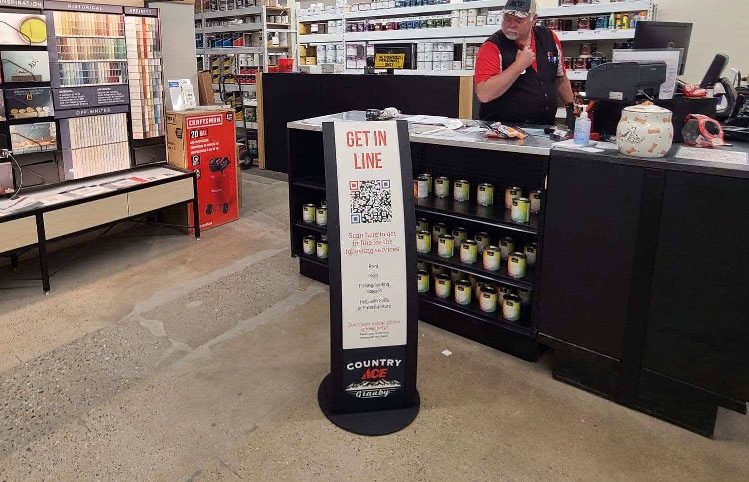 An Edge Curve retail sign stand with printed graphics marks the checkout queue at an ACE Hardware store.