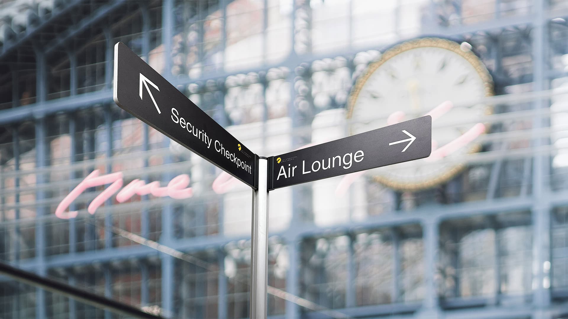 Tall partition posts with banner signs create directional street signs for wayfinding inside an airport terminal.