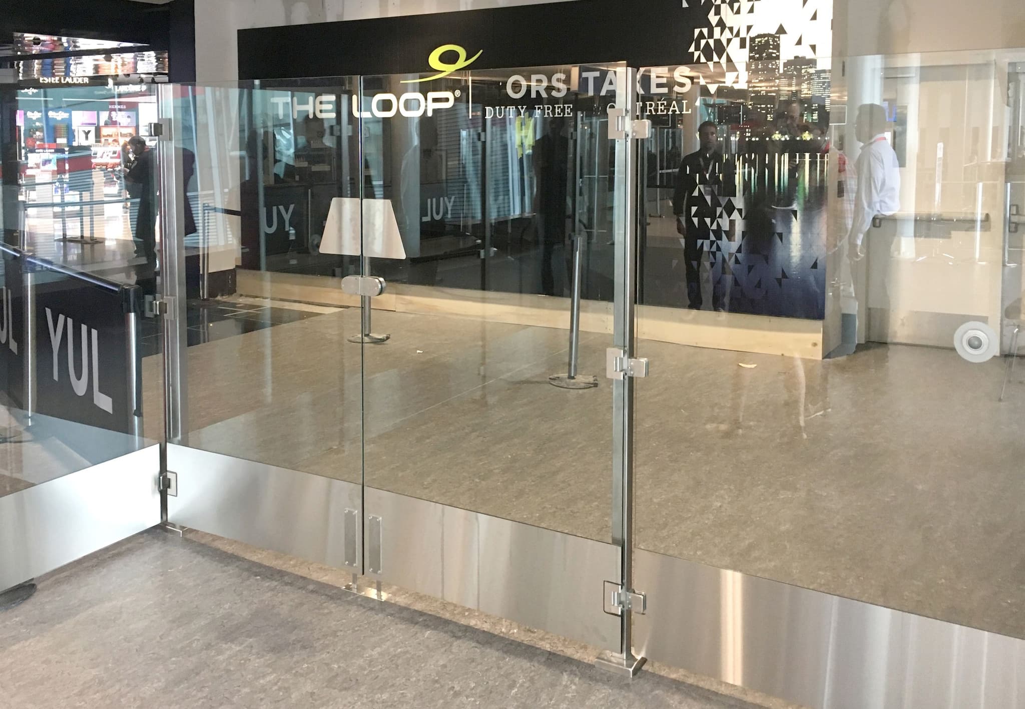 Tall glass Architectural Partition Walls with an access gate enclose a retail space inside an airport terminal.